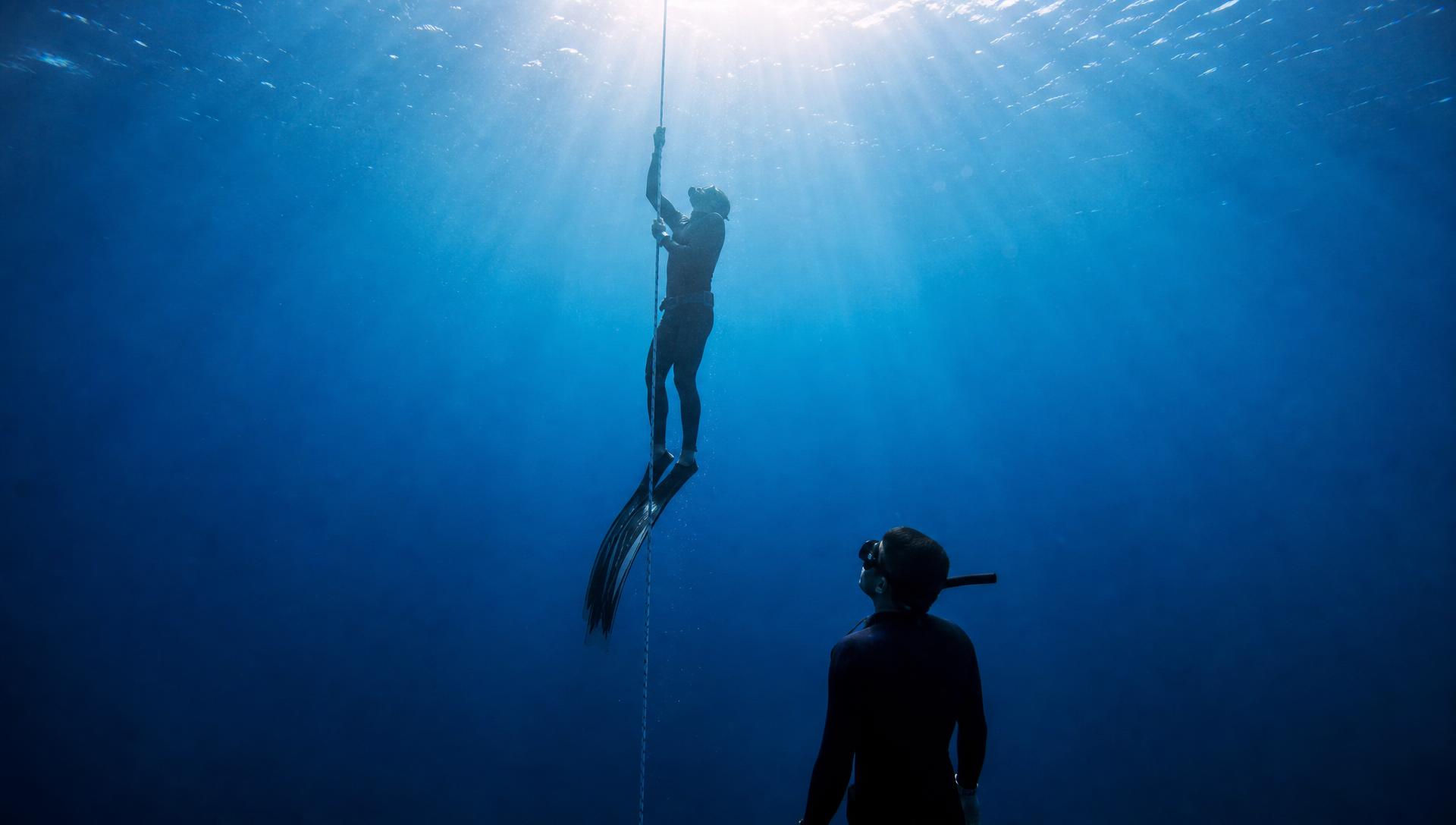 Freediver ascending a line while a safety diver watches